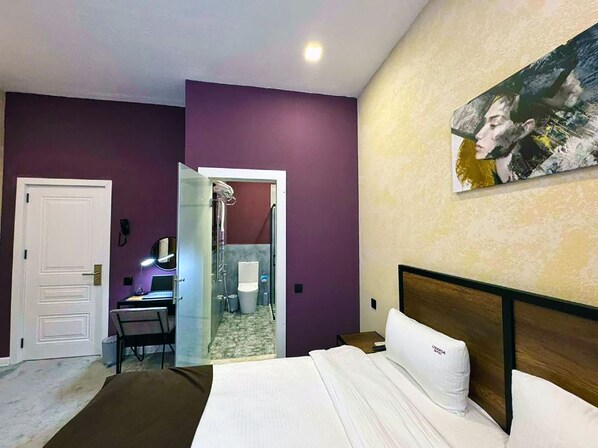 A hotel room with a bed, a desk, and a shower area.