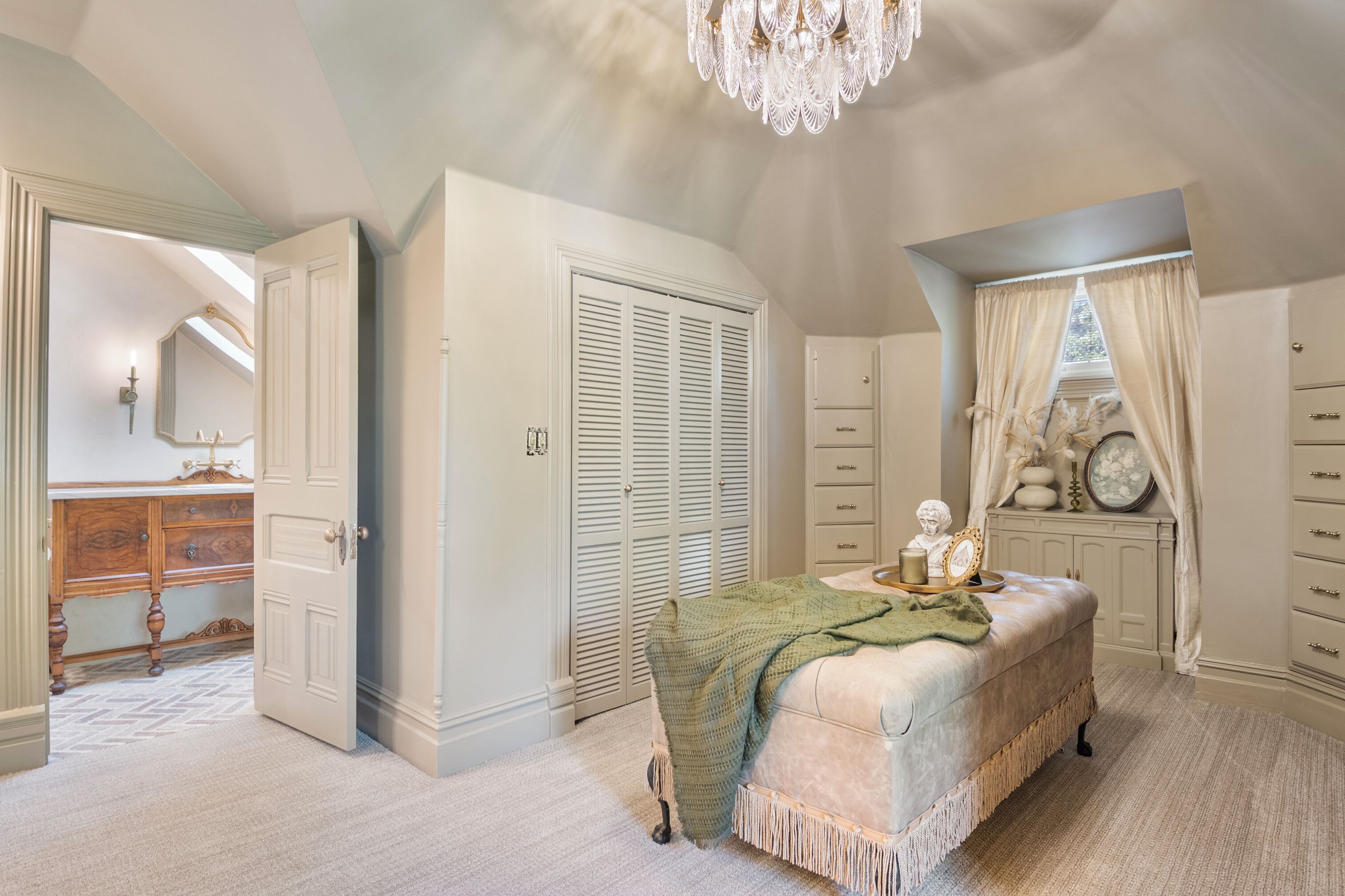 A bedroom with a large bed, a vanity with a mirror, a dresser, and a walk-in closet.