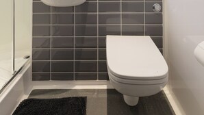 Et moderne badeværelse med en hvid vask, mørke flisevægge, et toilet og en brusekabine i glas.