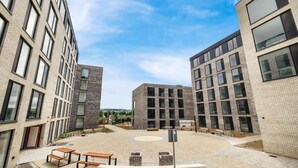 En gårdsplads med moderne bygninger, udendørs siddepladser og et åbent centralt område.