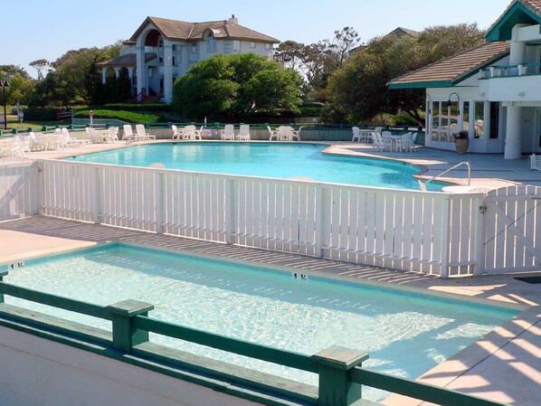 Una piscina con cerco blanco, sillas de descanso y una casa al fondo.