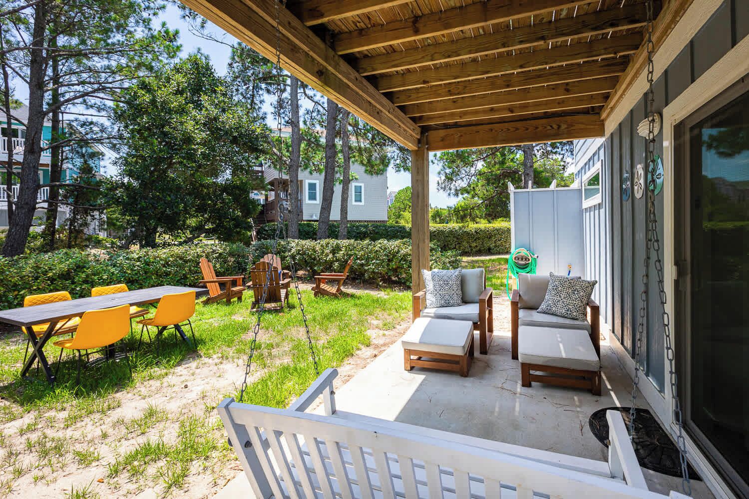 An outdoor patio with wooden furniture, including chairs and a table, and a swing set.