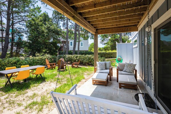An outdoor patio with wooden furniture, including chairs and a table, and a swing set.