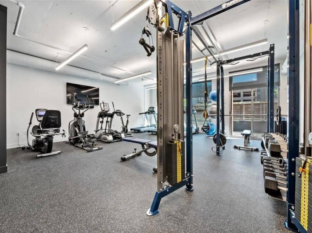 Et fitnesscenter med forskellig træningsudstyr, herunder en squat-stativ, løbebånd og styrkemaskiner.