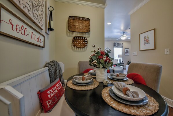 A dining area with a black table set for four, surrounded by chairs. There are decorative wall hangings and a vase with flowers on the wall.