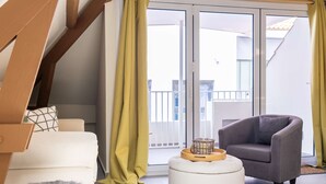 A modern living room with a sofa, armchair, ottoman, and a glass door leading to a balcony. - Bright Historic Loft in the Heart of Willemstad (Willemstad)