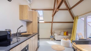 A compact living space with a kitchenette, a sofa, a dining table, and a small stool. - Bright Historic Loft in the Heart of Willemstad (Willemstad)