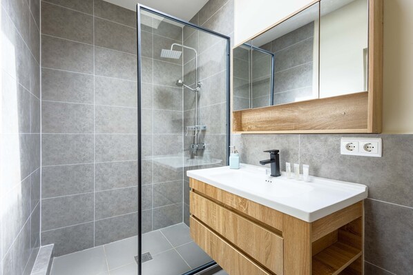 A modern bathroom with a glass-enclosed shower, a wooden vanity with a white countertop, and a large mirror above the vanity.