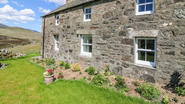 A stone house with multiple windows and a garden with various plants and flowers. - The Crannach (Blairgowrie)
