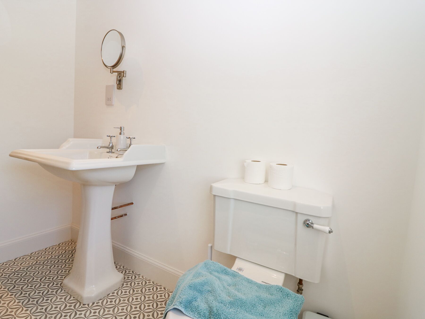 A bathroom with a pedestal sink, toilet, and a blue towel on the floor.