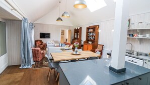 A spacious living area with a wooden dining table, a kitchen with a built-in island, and a cozy seating area with patterned curtains. - The Crannach (Blairgowrie)