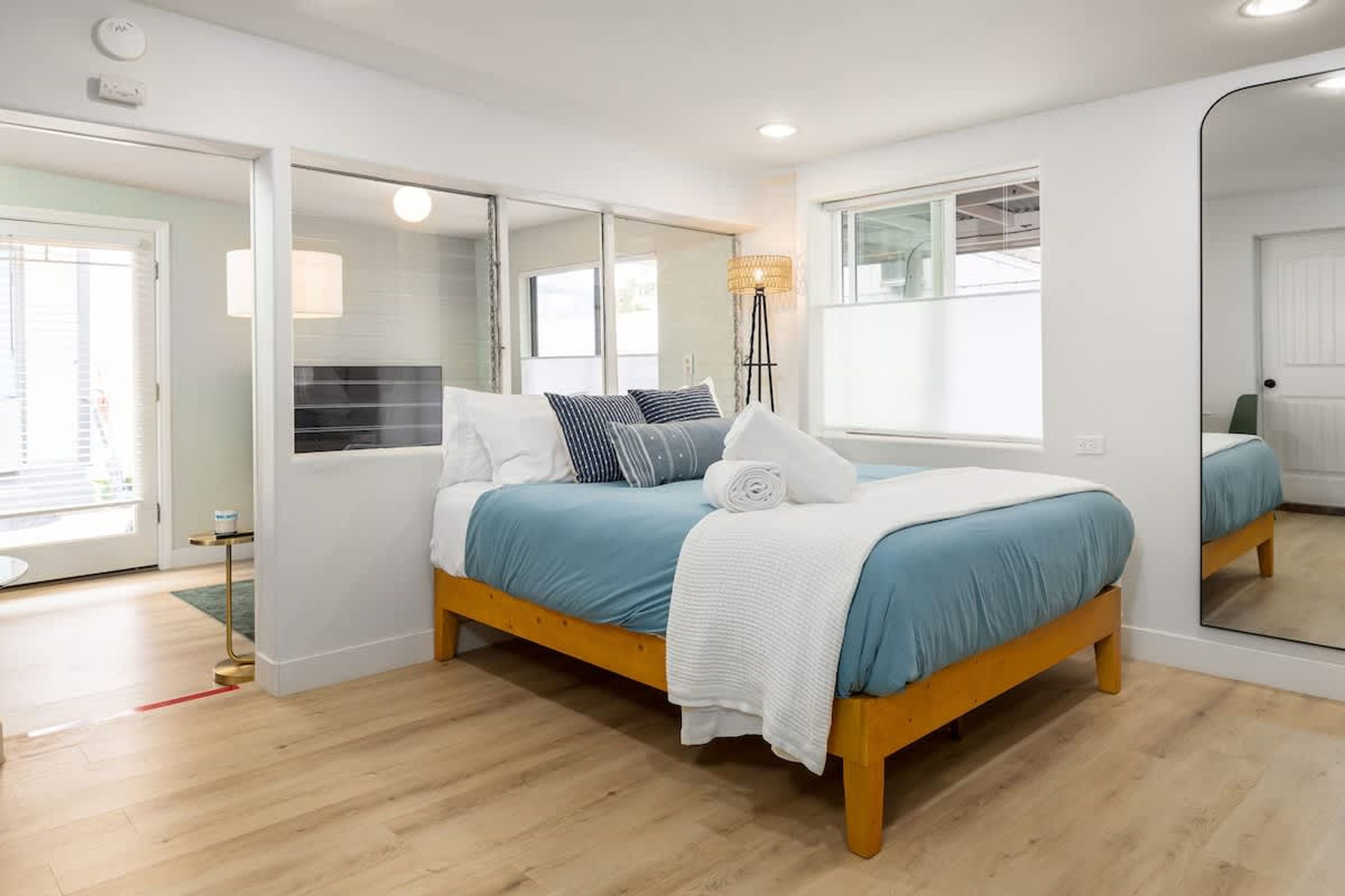 A bedroom with a bed, a mirror, a floor lamp, and a window.