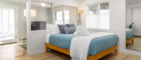 A bedroom with a bed, a mirror, a floor lamp, and a window.