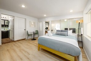A bedroom with a bed, bedside table, chair, and a view of the bathroom. - Studio In Carlsbad Village (Carlsbad)
