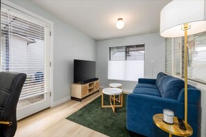 A living room with a blue sofa, a TV, a lamp, and a small table with a remote.