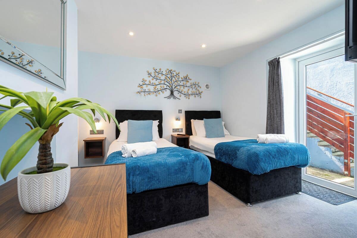 A modern bedroom with two beds, a large potted plant, and a decorative tree wall art.