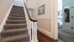 A staircase with carpeted steps and white balusters, leading to a room with a bed and a mirror on the wall.
