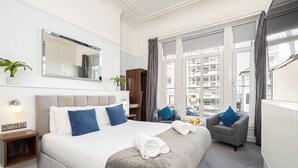 A hotel room with a large bed, a chair, a nightstand, a mirror, and a view of the city.