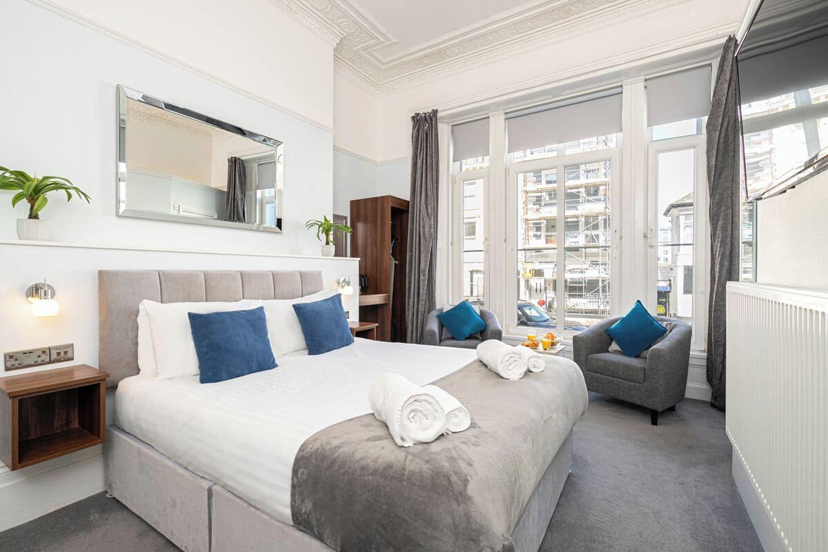 A hotel room with a large bed, a chair, a nightstand, a mirror, and a view of the city.