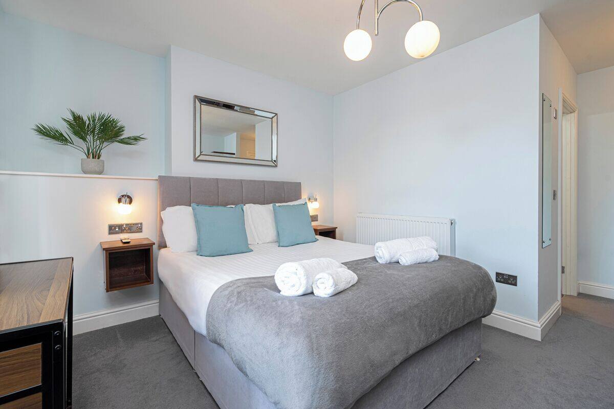 A neatly arranged bedroom with a bed, bedside tables, a mirror, and a potted plant.
