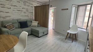 Una sala de estar moderna con un sofá seccional gris, una mesa de comedor de madera con sillas blancas y una silla blanca junto a la ventana.