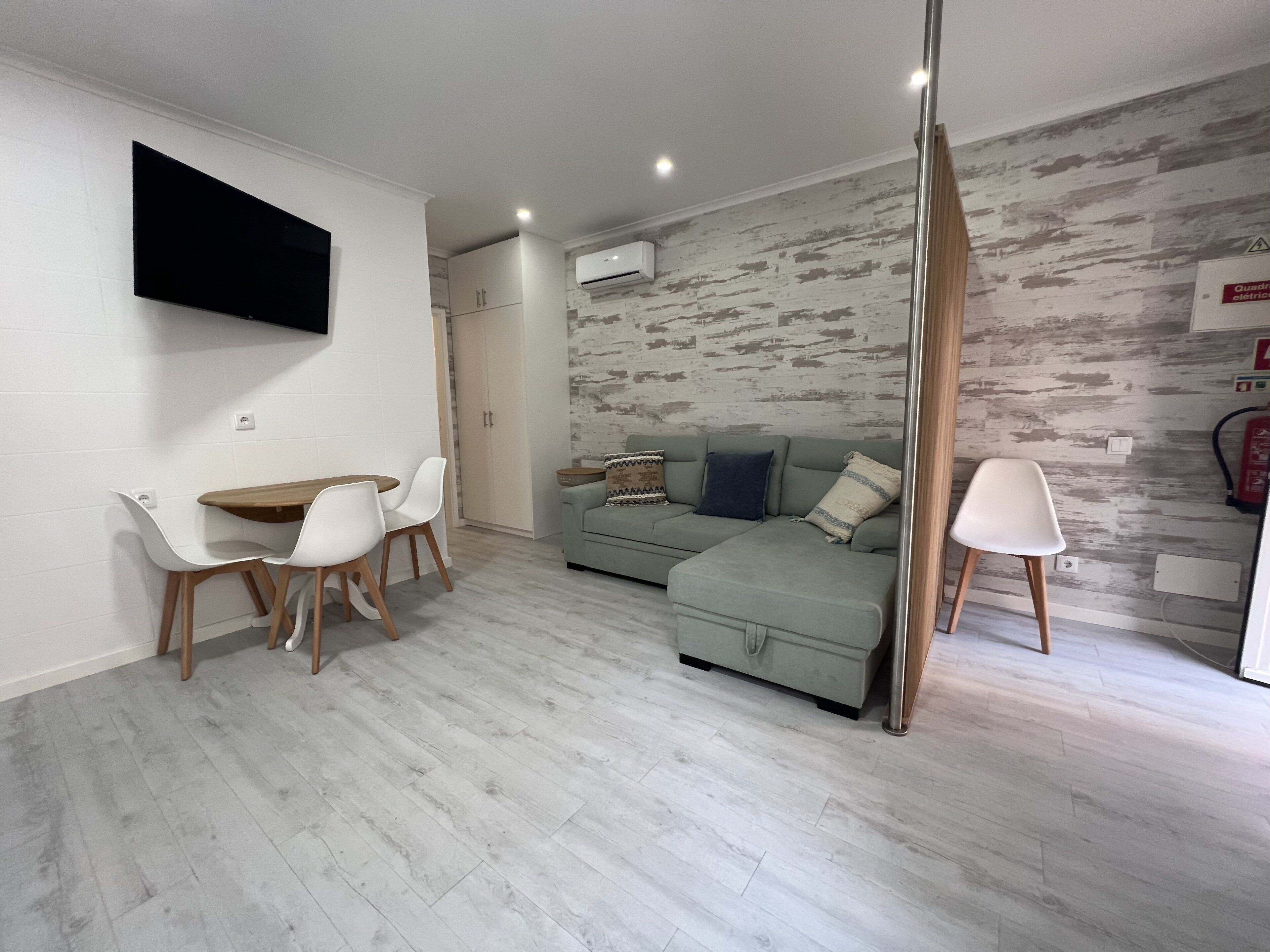 A modern living room with a dining area, a sofa set, and a flat-screen TV mounted on the wall.
