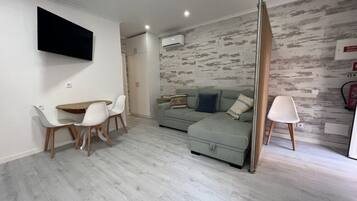 A modern living room with a dining area, a sofa set, and a flat-screen TV mounted on the wall.