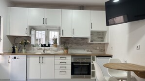 Una cocina moderna con armarios blancos, horno integrado, lavavajillas y un comedor con mesa de madera y sillas blancas.