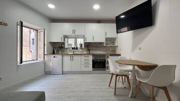 A modern kitchen with white cabinets, a built-in oven, and a dining area with a wooden table and white chairs.