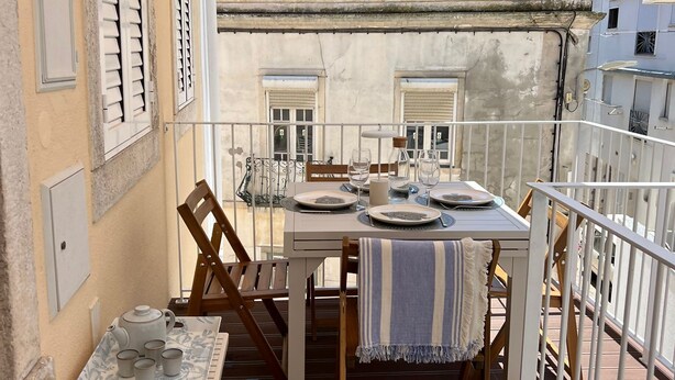 Un balcon avec une table dressée pour le repas, des chaises et une petite table sur laquelle se trouvent des tasses et une théière.