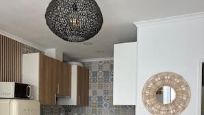 Une cuisine compacte équipée d’un four à micro-ondes, d’une cuisinière et d’un évier. On y trouve un meuble en bois, un tabouret et un miroir accroché au mur.