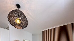 Un salon moderne doté d’un grand téléviseur à écran plat, d’un luminaire suspendu en fibres tressées et d’un panneau mural en bois.