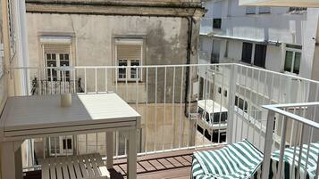 A balcony with a white table and bench, a striped cushion, and a view of adjacent buildings.