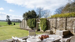 A round wooden table with chairs, a teapot, cups, and a tray set outdoors with a stone wall and greenery in the background. - The West Wing, Capheaton in Northumberland - sleeping 8 guests in 4 bedrooms (Capheaton)