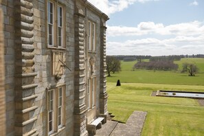 A stone building with a clock, large windows, and a view of a green field and trees. - The West Wing, Capheaton in Northumberland - sleeping 8 guests in 4 bedrooms (Capheaton)