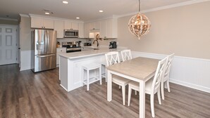 Une cuisine moderne avec des meubles blancs, des appareils en acier inoxydable et une table à manger en bois, assortie de chaises blanches.
