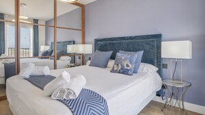 Habitación de hotel con una cama grande, un espejo, una mesita de noche con lámpara y vistas a la ciudad.