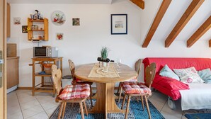 Ein gemütliches Zimmer mit Esstisch, Stühlen, einer roten Couch und einer Holzbalkendecke.