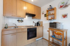 A kitchen with wooden cabinets, a built-in oven, a microwave, and a shelf with kitchenware.