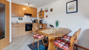 Eine Küche mit Holzausstattung, einem Esstisch mit Stühlen und einem an der Wand befestigten Regal mit Dekoration.