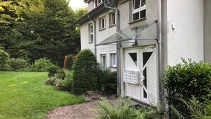 Ein Wohngebäude mit gepflasterter Auffahrt, einem befestigten Eingangstor und einem gepflegten Garten mit unterschiedlichen Pflanzen und einem kleinen Teich.