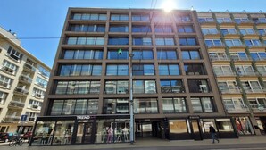 Un edificio de varios pisos con un diseño arquitectónico moderno, que cuenta con espacios comerciales en la planta baja con escaparates visibles.