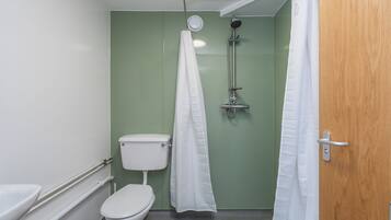 A small bathroom with a toilet, a shower, and a wooden door.