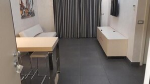 A compact hotel room with a bed, a small desk, a chair, and a TV mounted on the wall. - FULL HOME. (Cosenza)