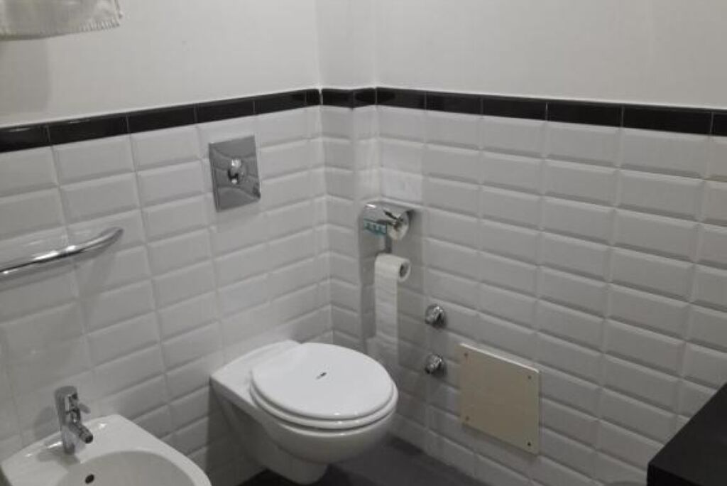 Un baño pequeño y limpio con azulejos blancos, un inodoro, un bidé y un perchero para toallas.