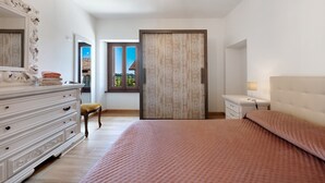 Un dormitorio con una cama grande, un aparador, un espejo, una ventana con vistas y una puerta de madera.