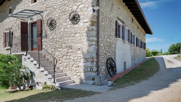 Un edificio de piedra con una escalera, una rueda y un banco.