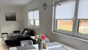 A modern living room with a dining area, a sofa, a coffee table, and a view of the outside through large windows. - OsWALD Holiday Apartment (Ettenheim)