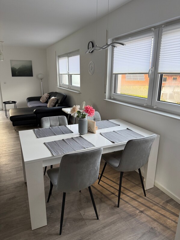 A modern living room with a dining area, a sofa, a coffee table, and a view of the outside through large windows. - OsWALD Holiday Apartment (Ettenheim)