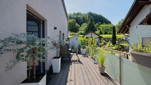A wooden deck with potted plants, a table with chairs, and a view of a green landscape in the background. - OsWALD Holiday Apartment (Ettenheim)